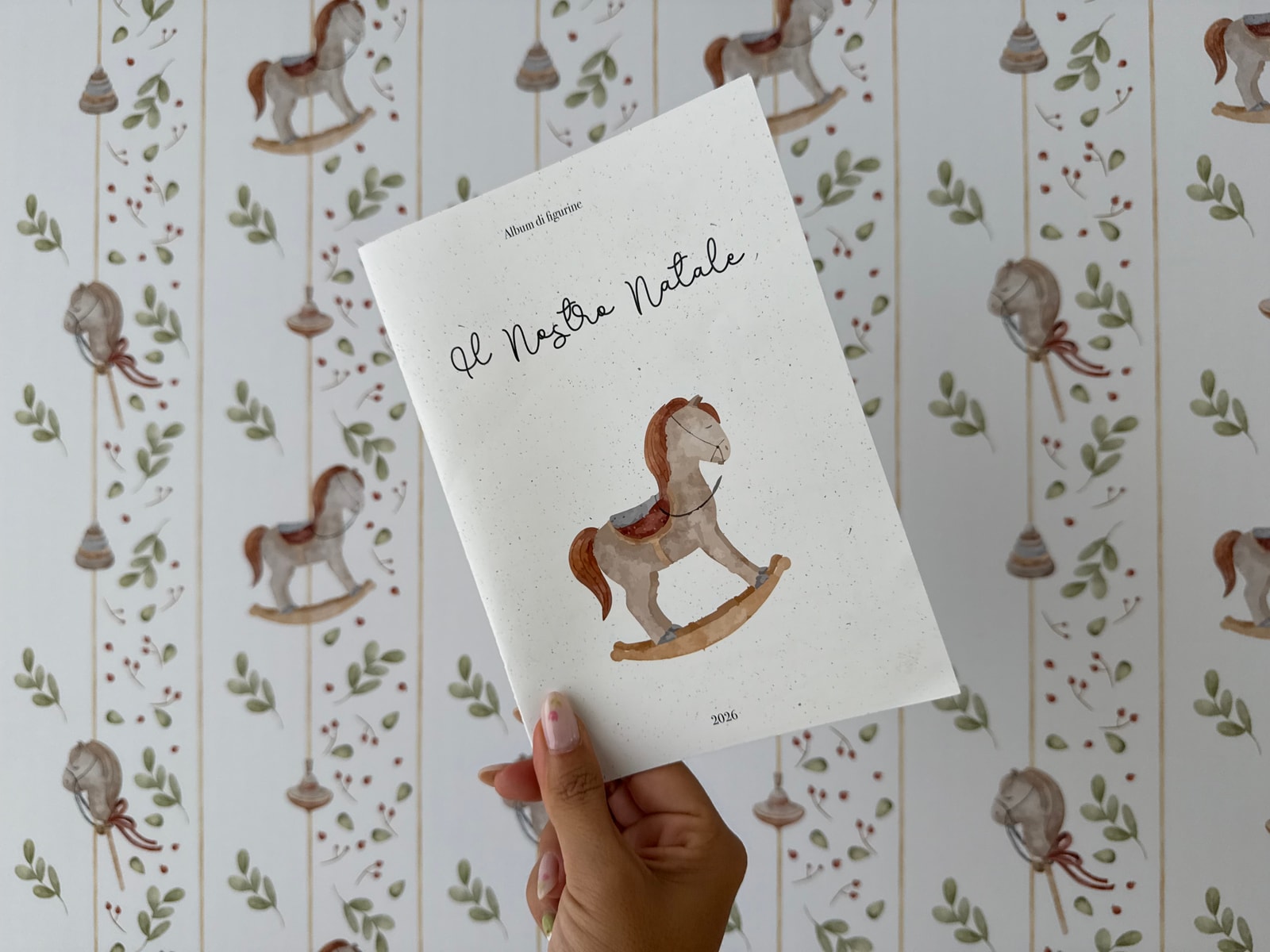Il libretto «Il Nostro Natale» tenuto in mano davanti alla carta da parati dello studio