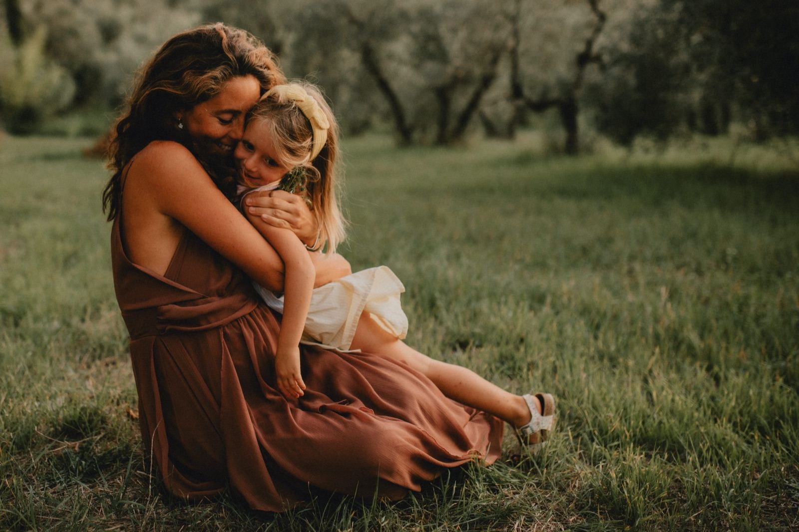 Mamma e bambina abbracciate in un prato al tramonto
