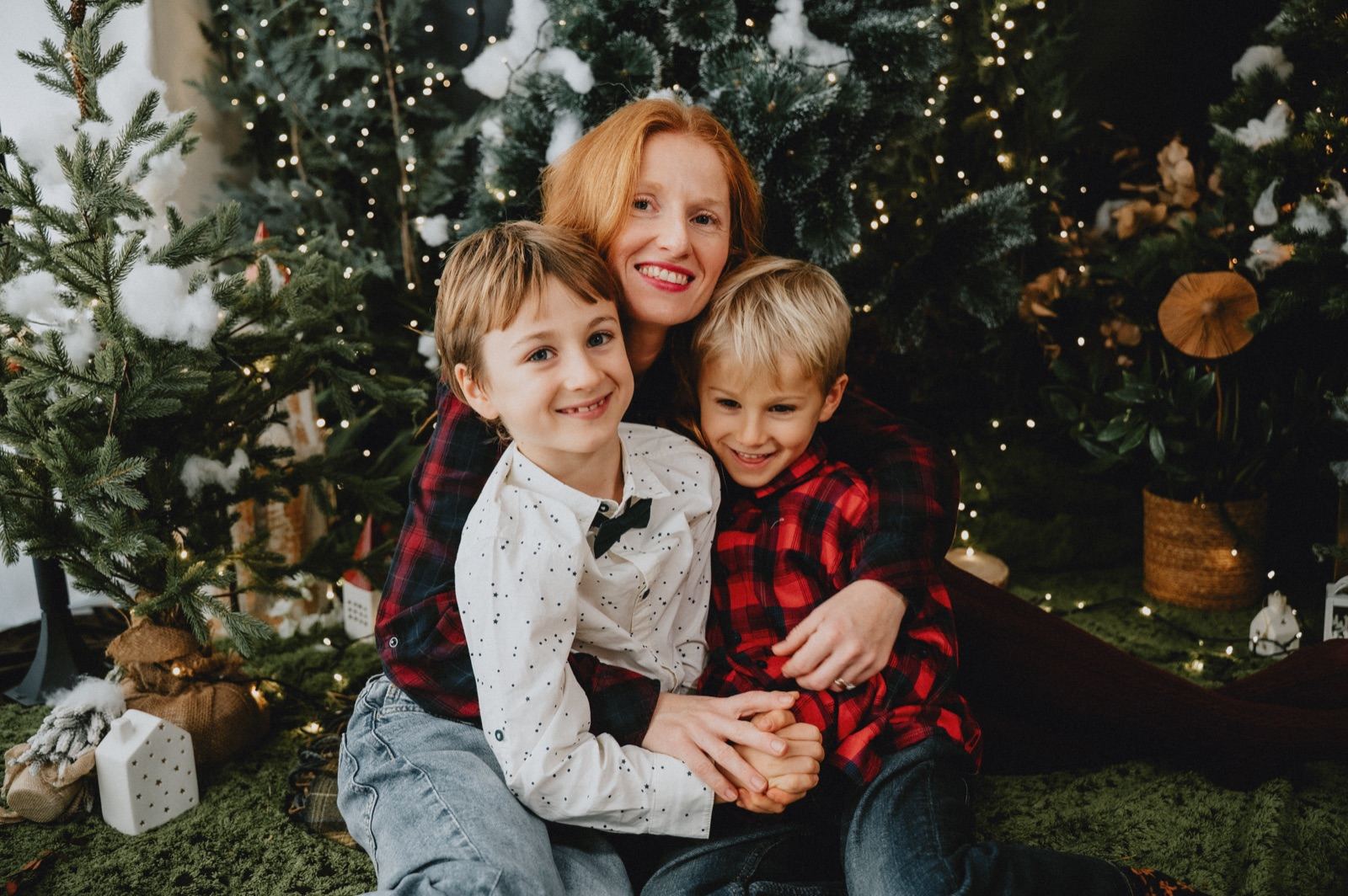 Mamma con i due figli in camicia a quadri e maglia bianca, fra gli abeti