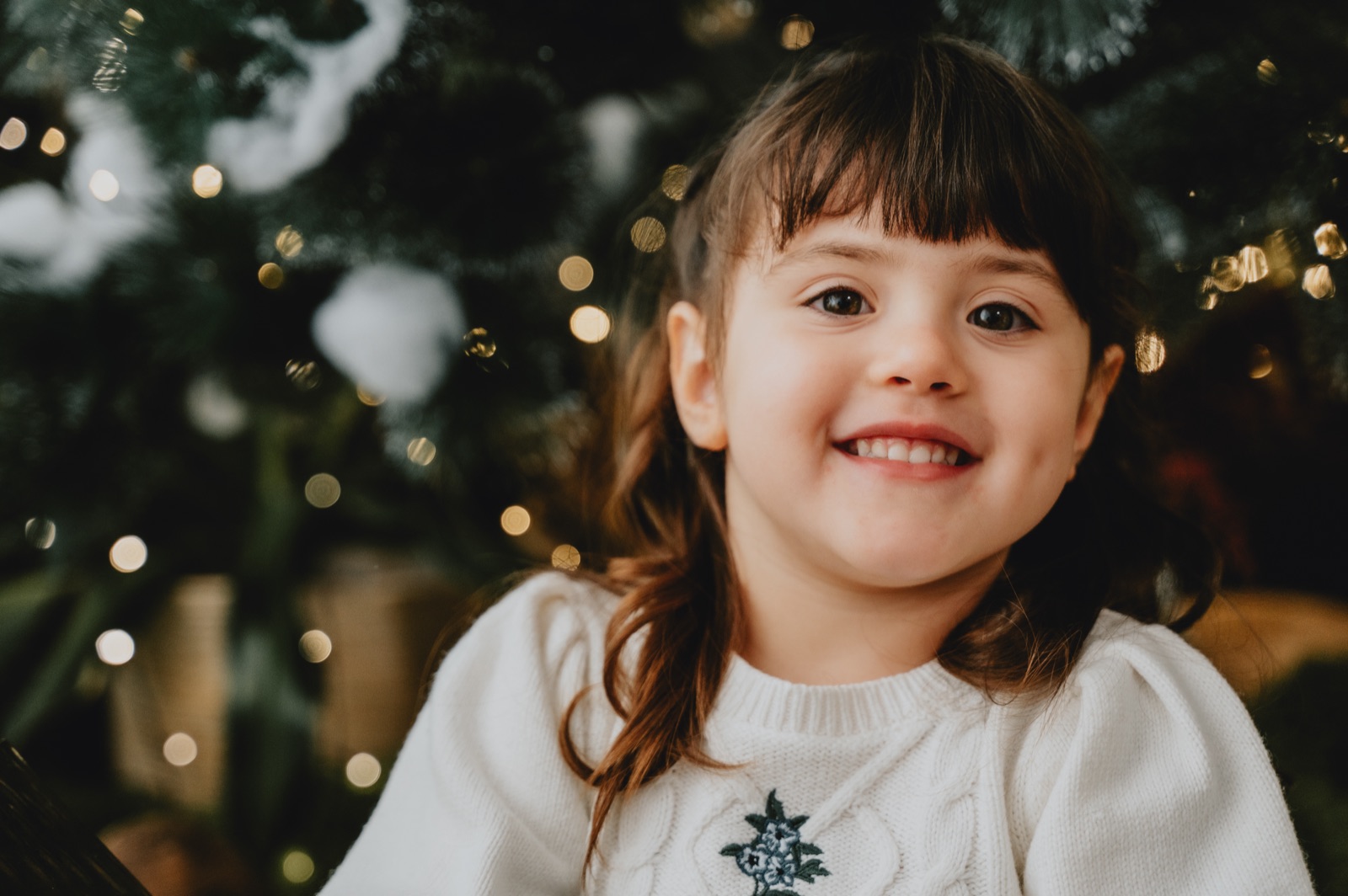 Bambina in maglia bianca con il fiocco di neve, le luci sfocate alle spalle