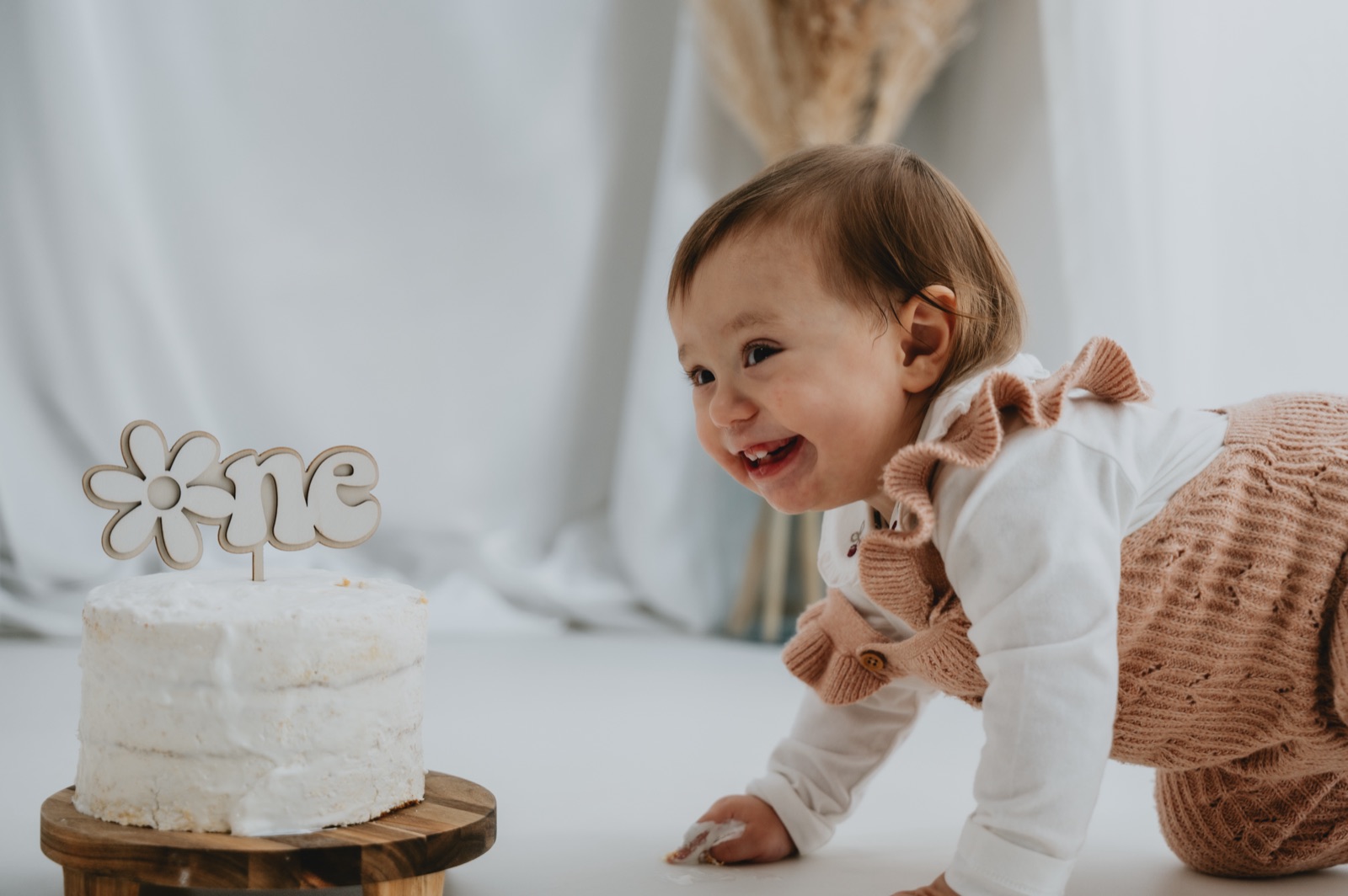 Bambina che si avvicina gattonando alla torta bianca con il cake topper