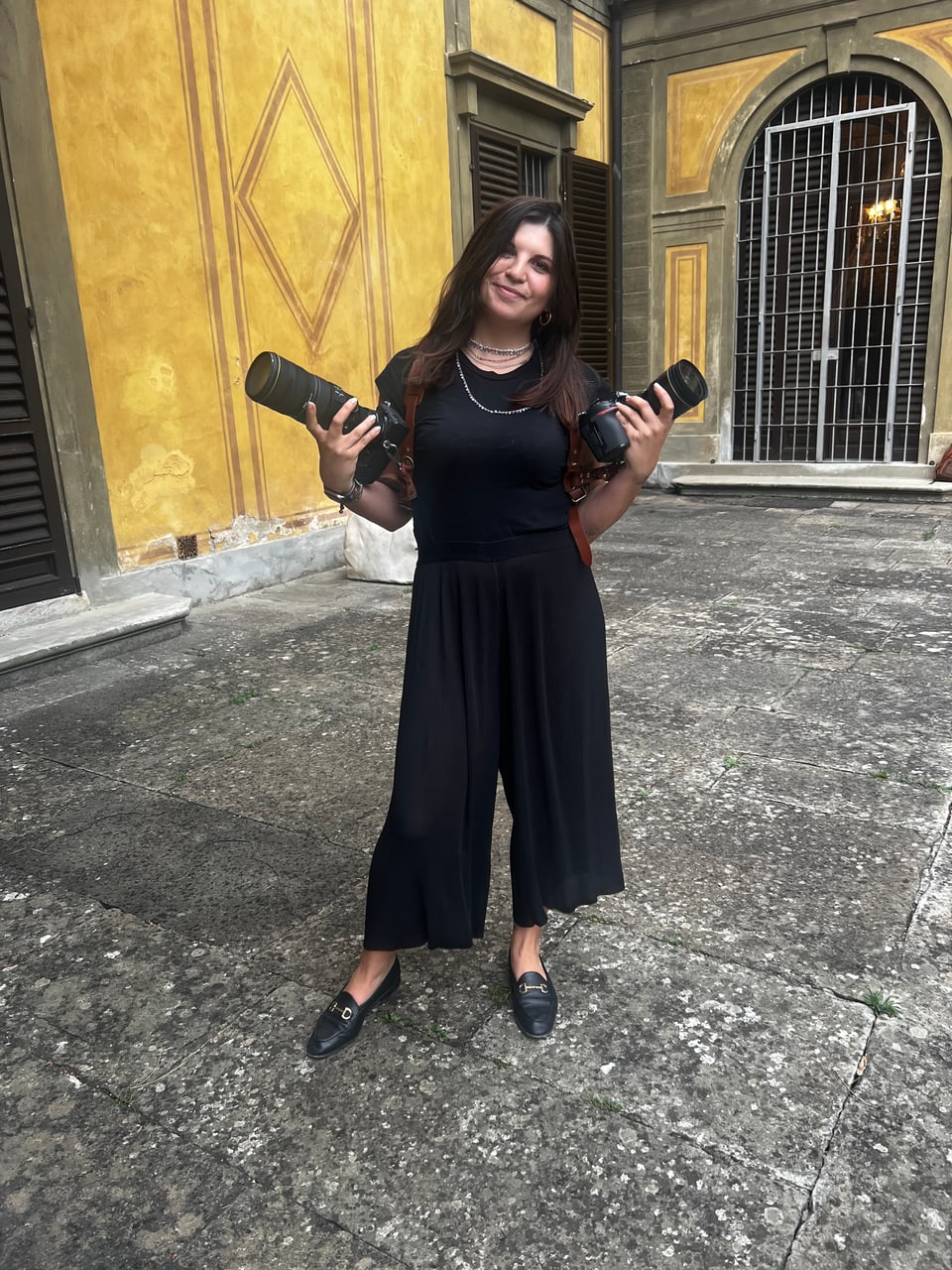 Virginia in piedi in un cortile di Firenze, con due obiettivi in mano