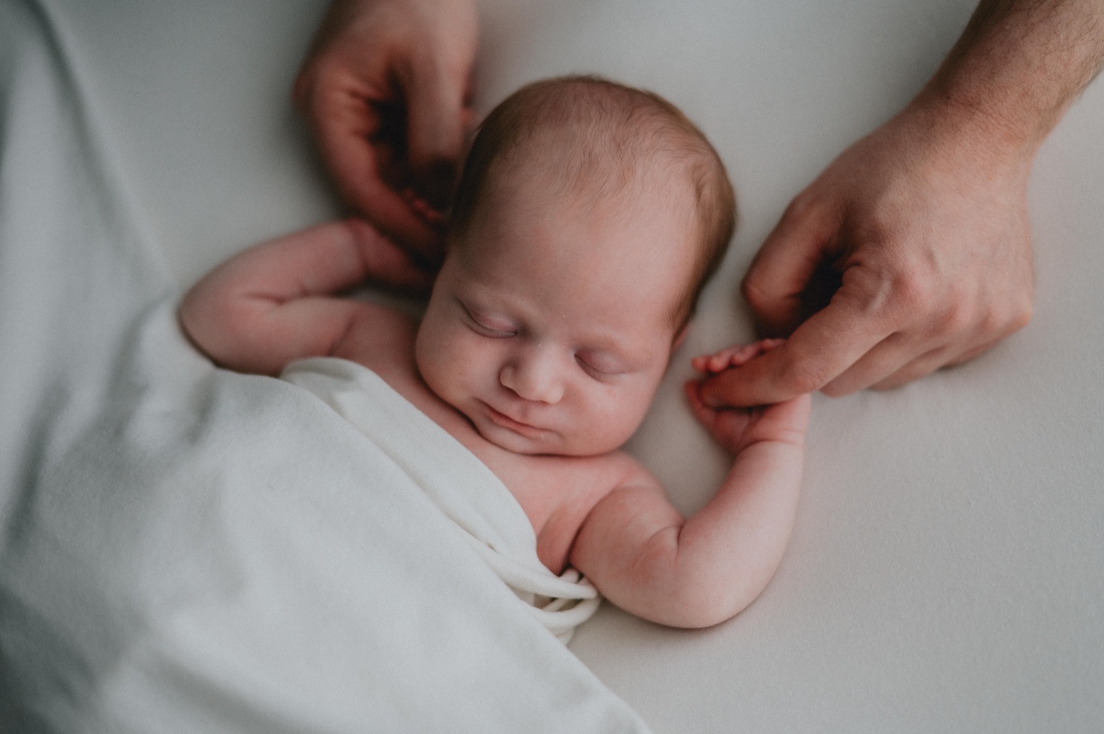 Neonato fra le mani dei genitori, su un telo chiaro