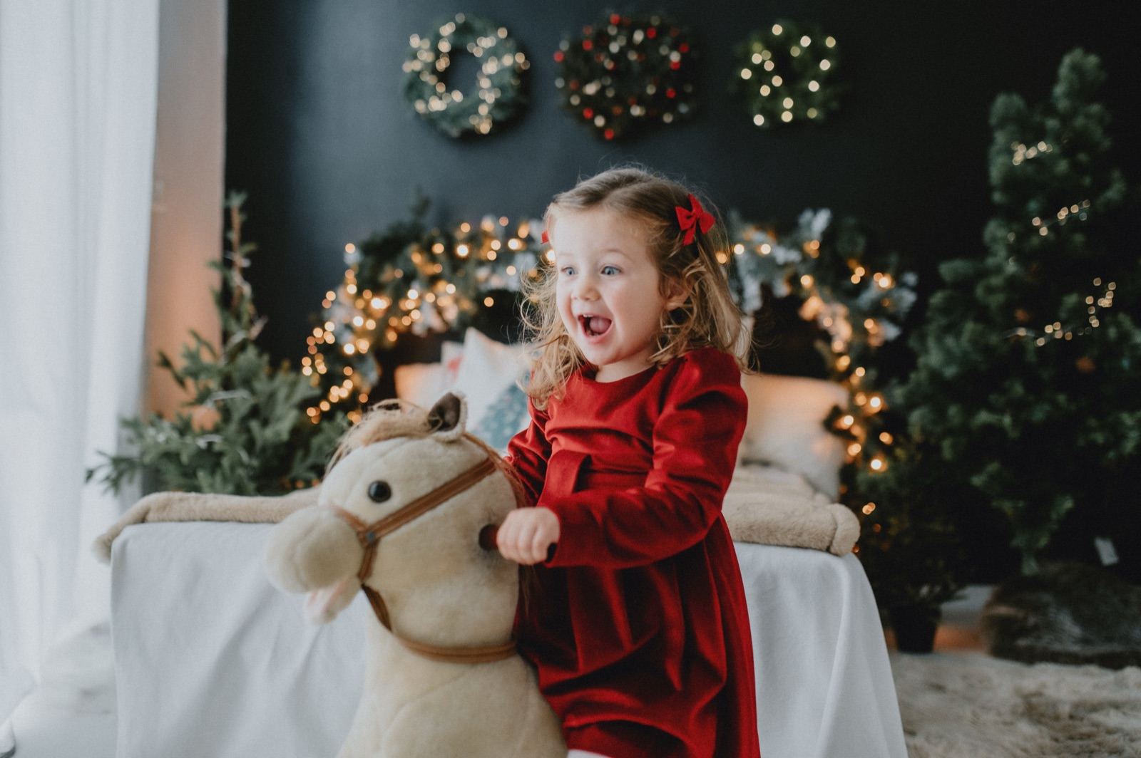 Bambina in abito rosso accanto a un cavallo a dondolo