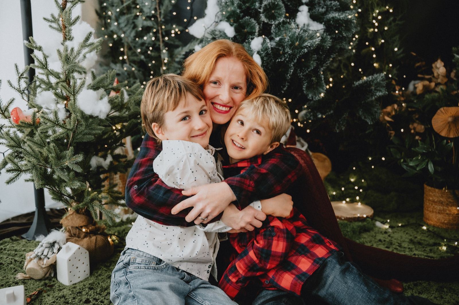 Mamma che abbraccia i due figli davanti agli abeti decorati