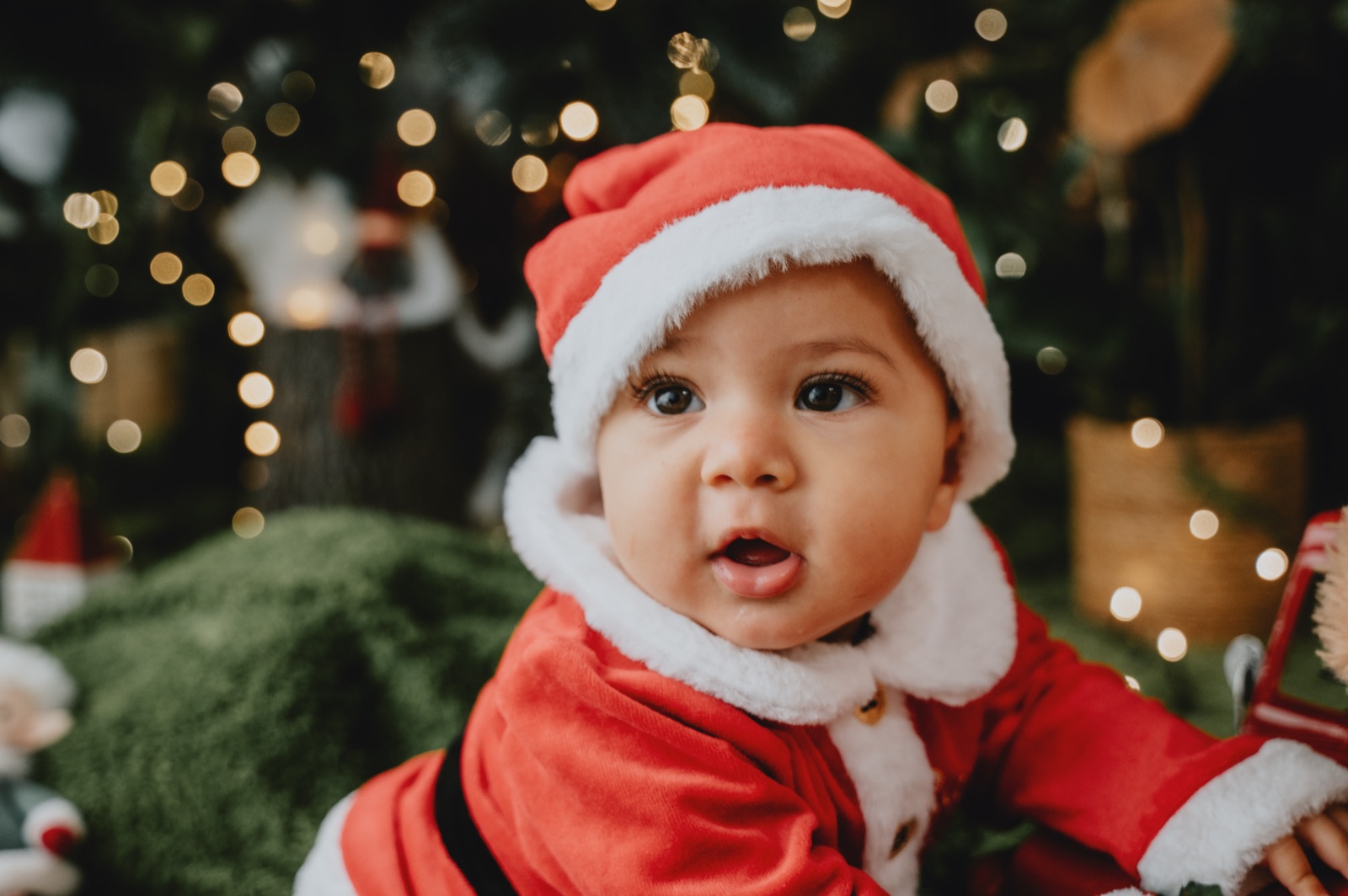 Bambino vestito da Babbo Natale che guarda l'obiettivo, le luci sfocate alle spalle