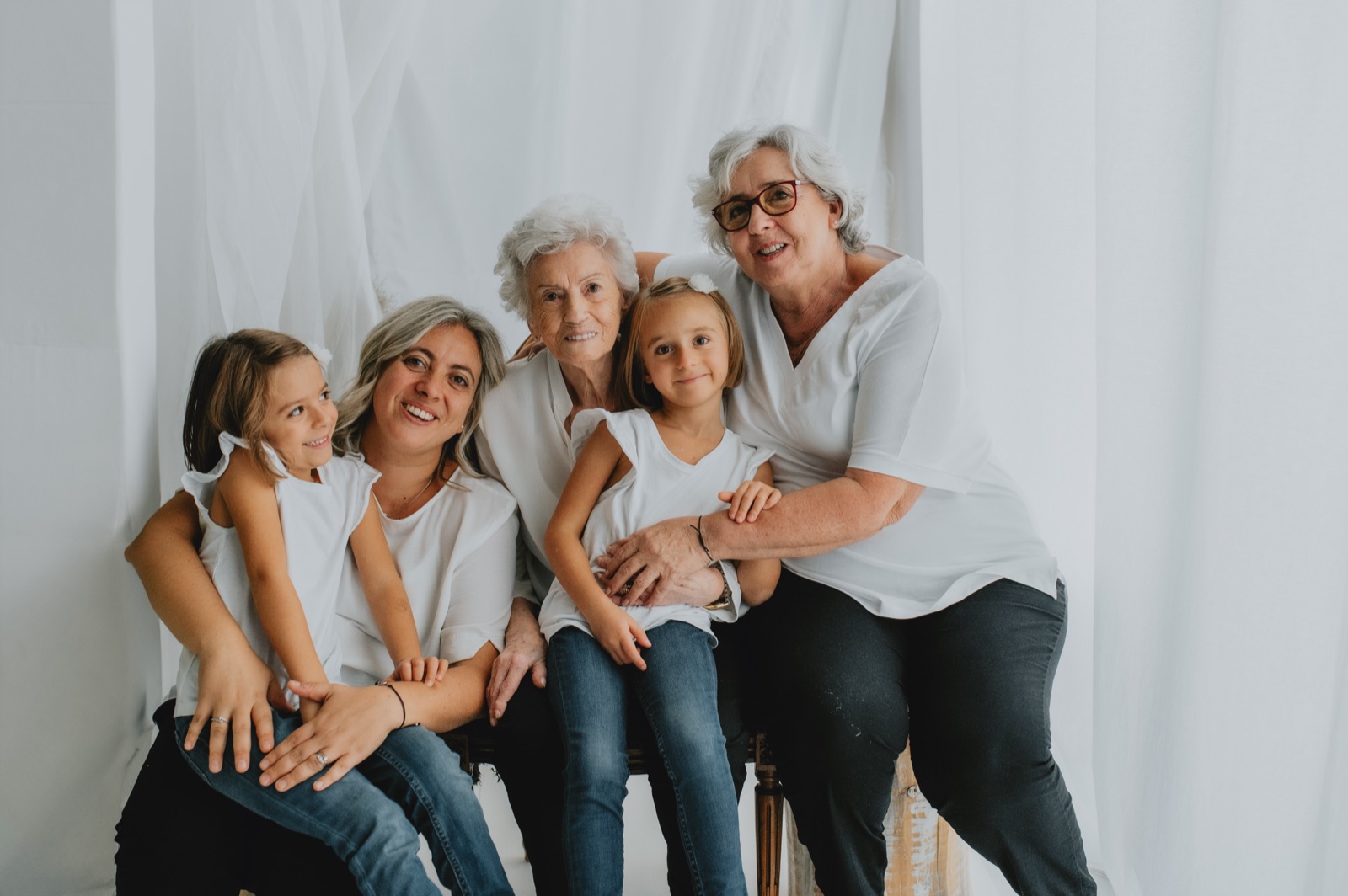 Quattro generazioni insieme davanti a un fondale chiaro: bisnonna, nonna, mamma e due bambine