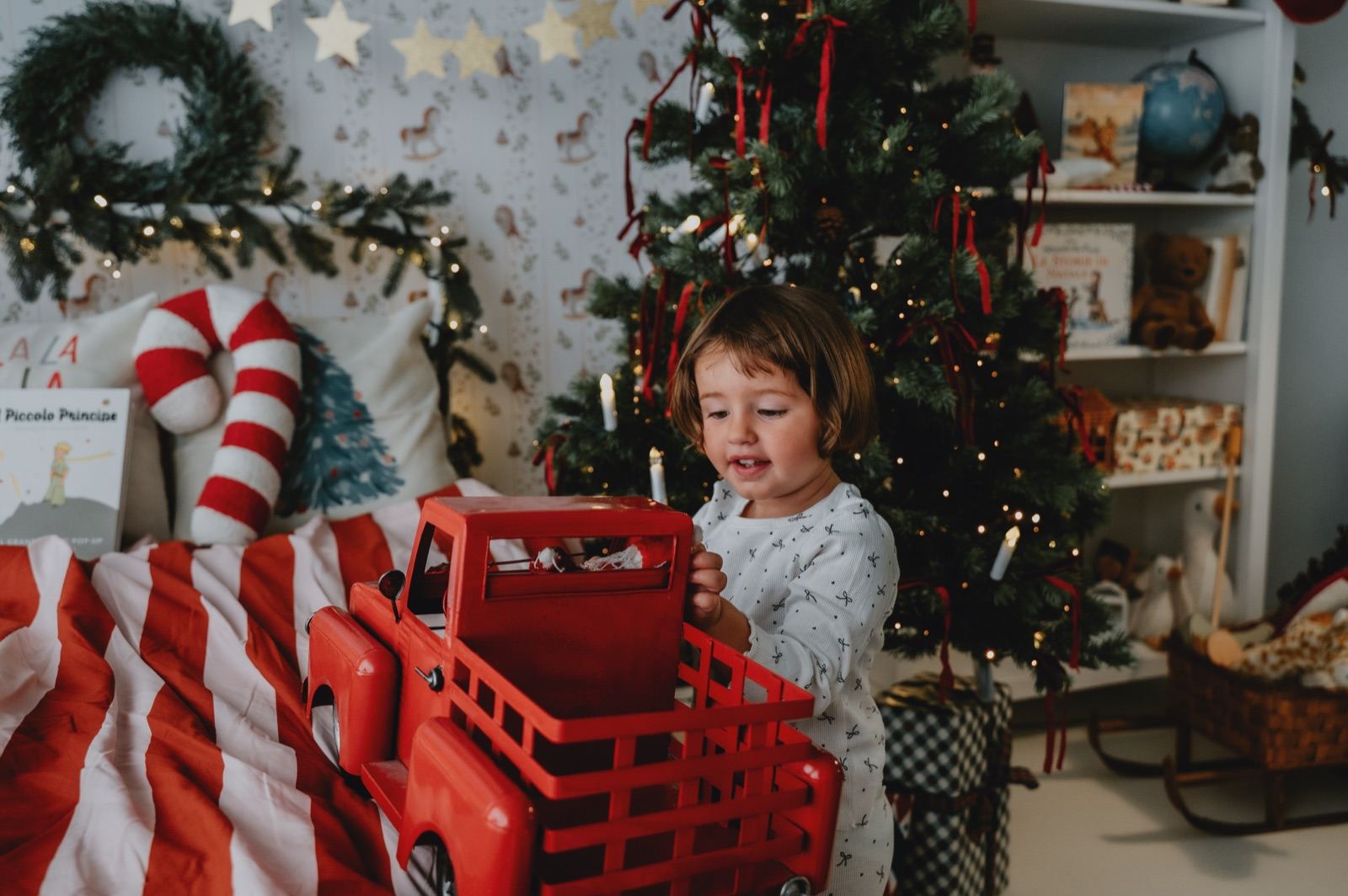 Bambina in pigiama che gioca con un camioncino rosso accanto all'albero di Natale
