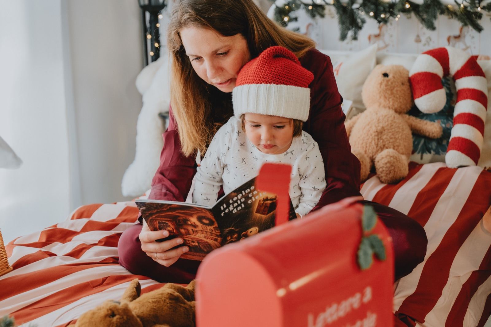 Mamma e bambina con il cappello di Babbo Natale che leggono un libro insieme sul letto
