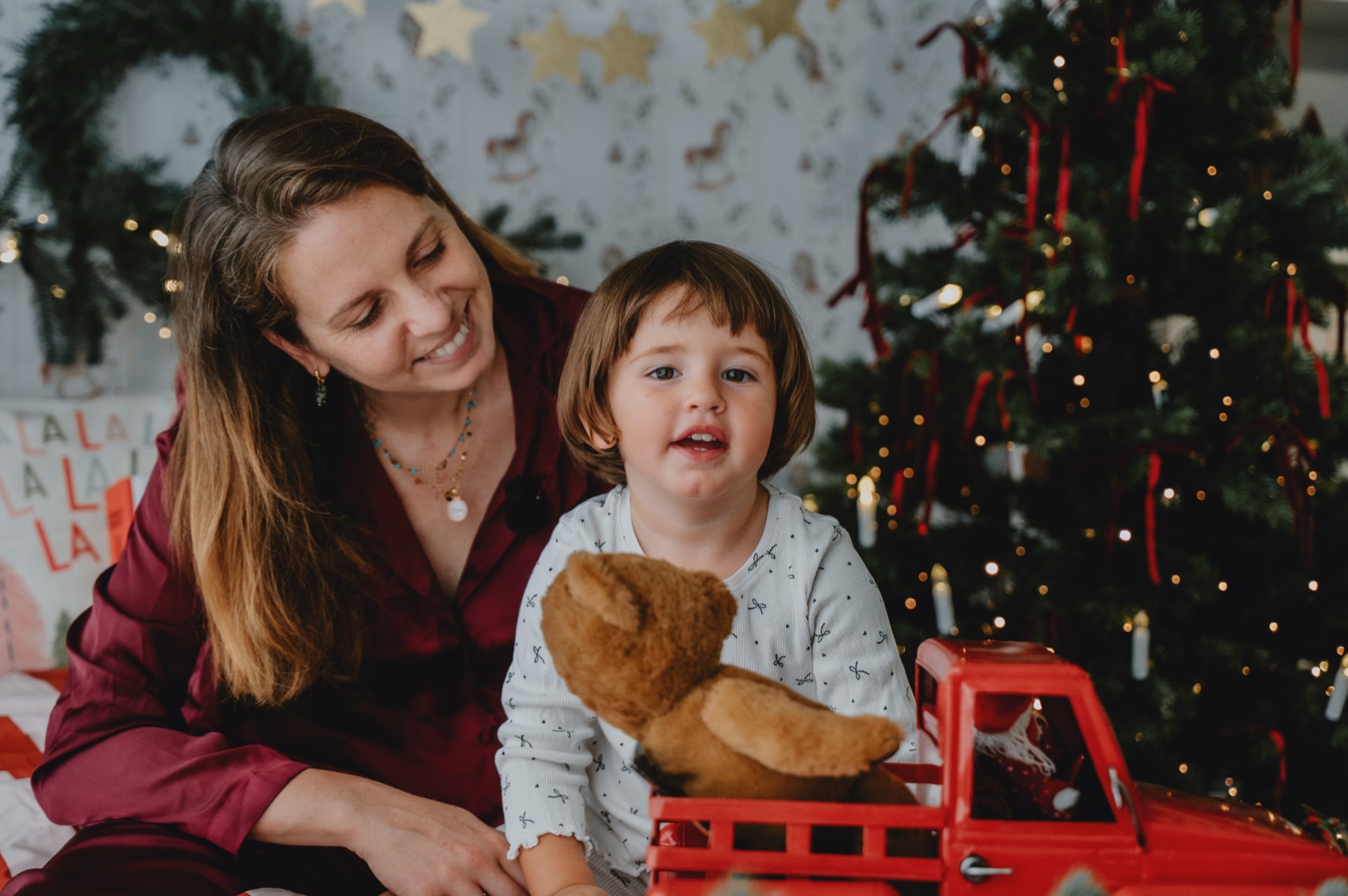 Mamma e bambina che ridono insieme accanto all'albero, con un orsetto in mano