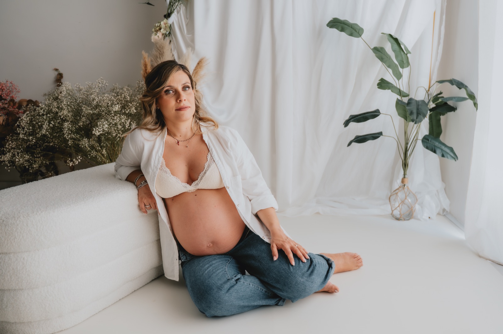 Futura mamma seduta a terra in studio, la camicia bianca aperta sul pancione