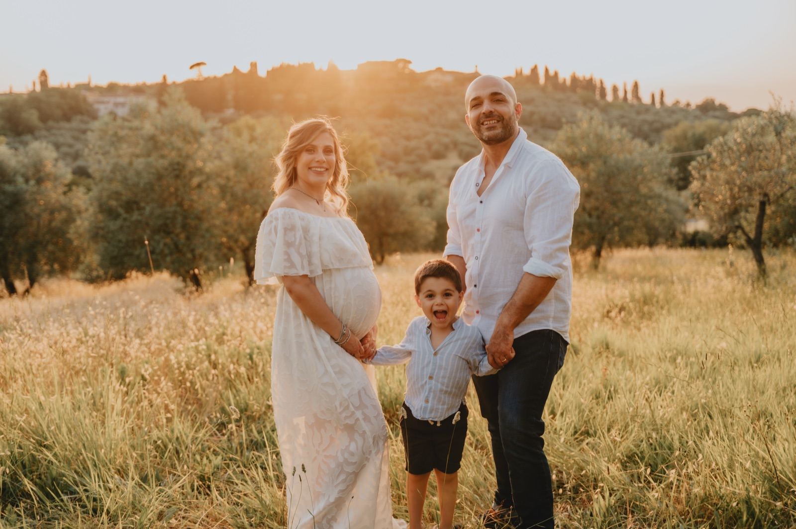 Famiglia in attesa con il figlio piccolo in un uliveto al tramonto