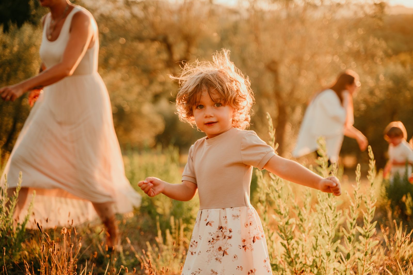 Bambina che corre in un campo mentre la mamma la segue, al tramonto