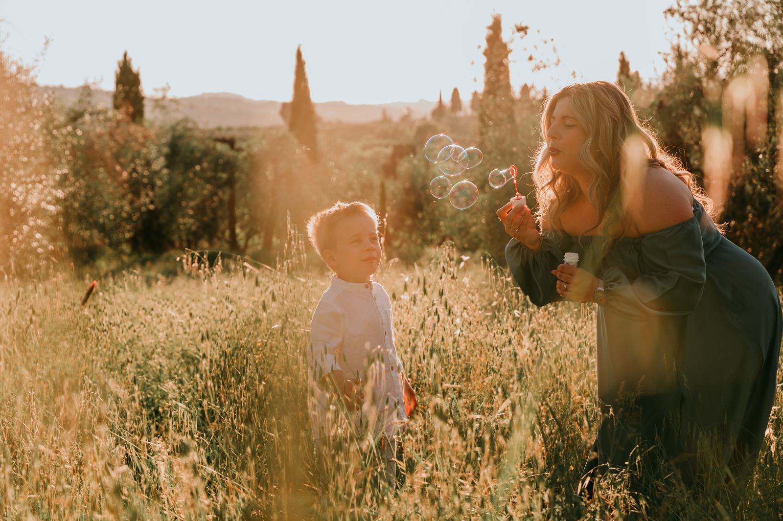 Mamma e bambino che soffiano un soffione in un campo al tramonto