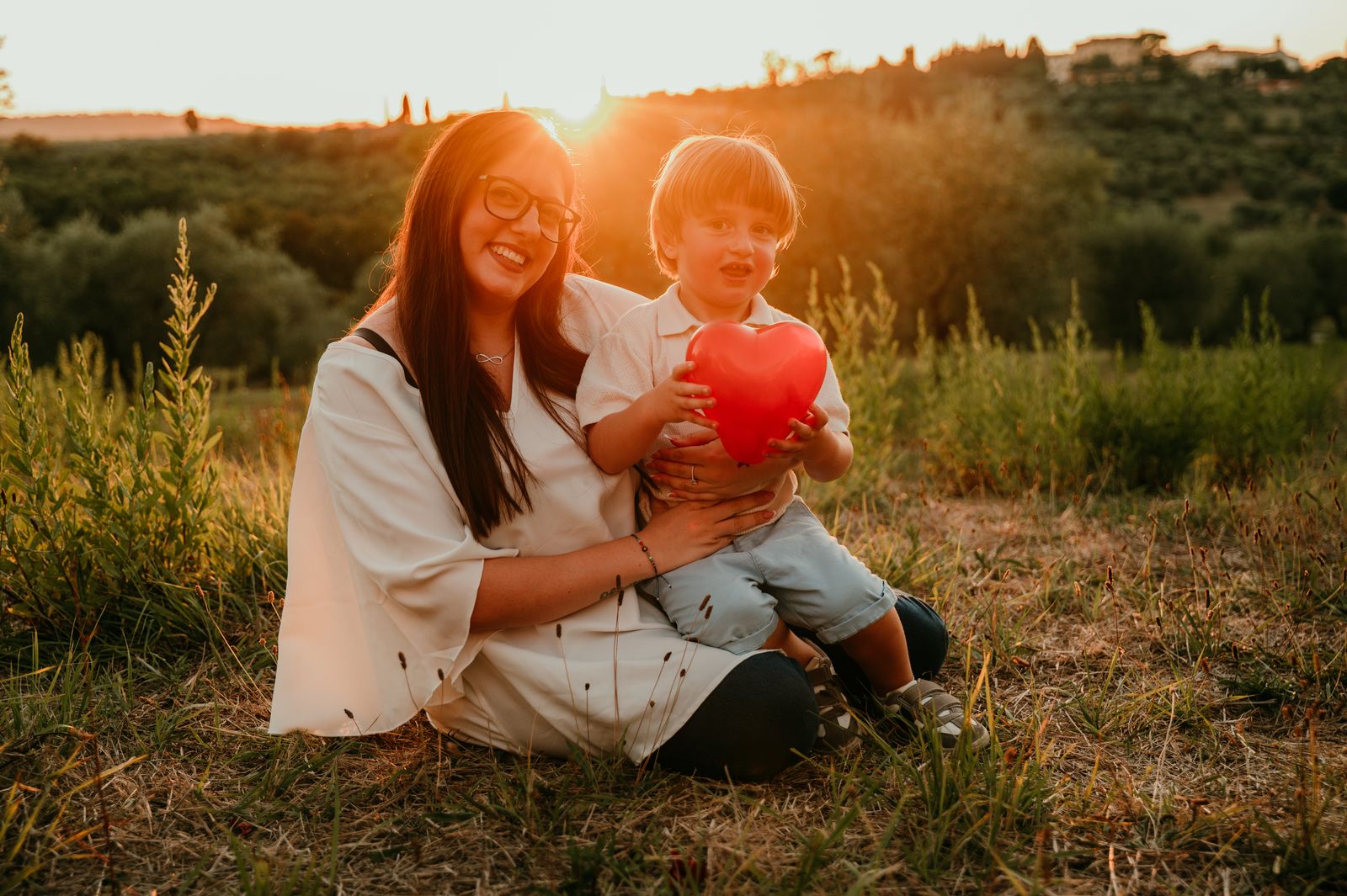 Mamma e bambino seduti nell'erba con la luce del tramonto alle spalle