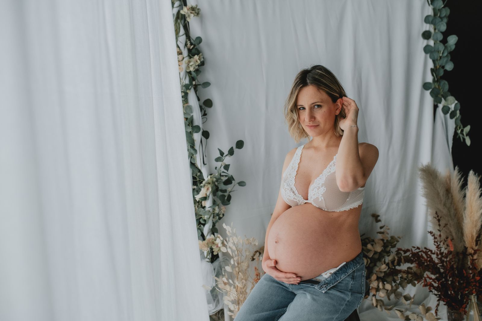 Futura mamma con top bianco e jeans, il pancione scoperto, in studio