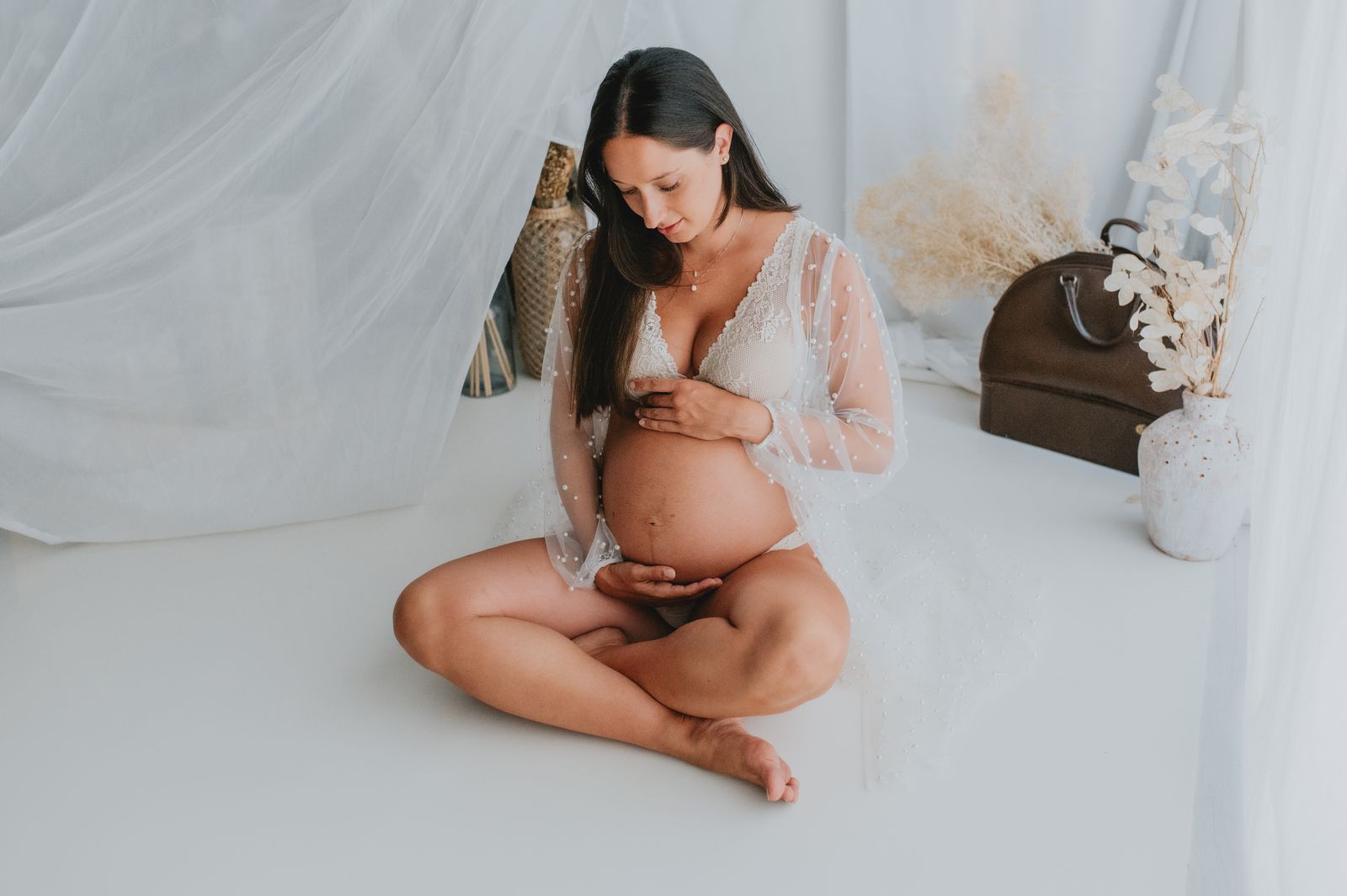 Futura mamma seduta a terra che accarezza il pancione nella luce naturale dello studio