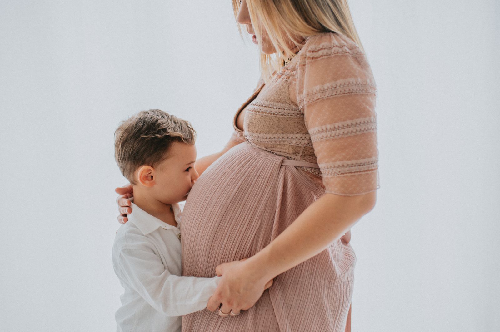 Bambino che appoggia le labbra sul pancione della mamma