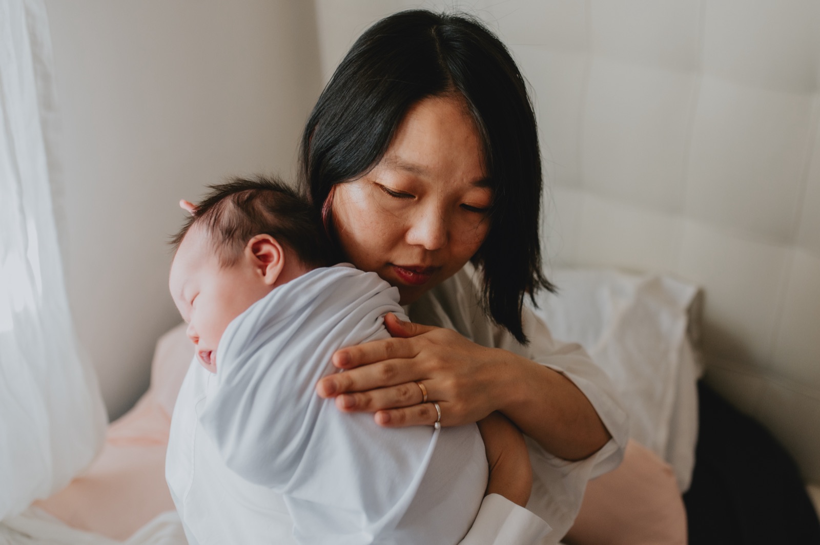Mamma che tiene il neonato addormentato appoggiato alla spalla, a casa