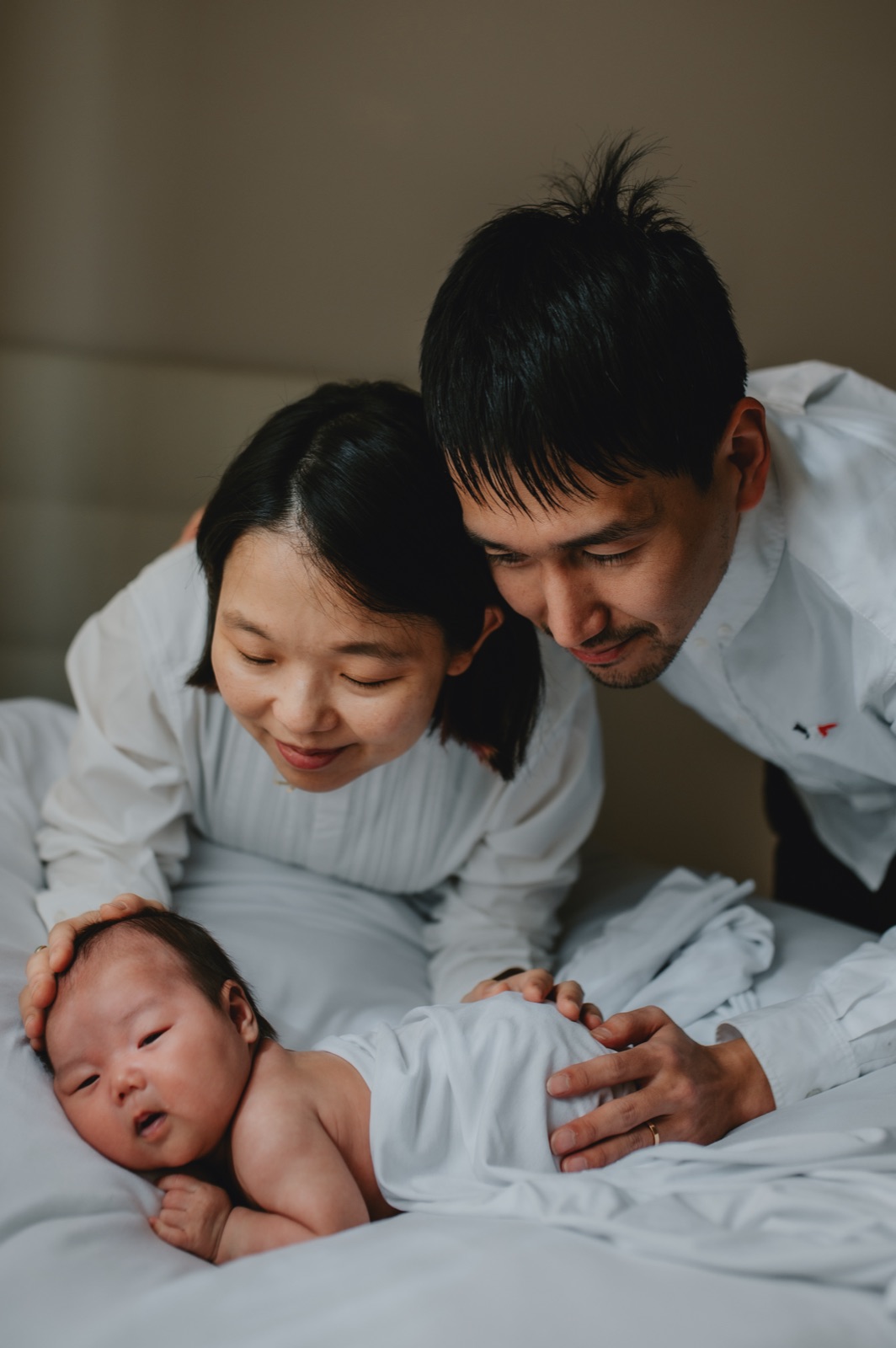 Mamma e papà chinati sul neonato sdraiato sul letto di casa