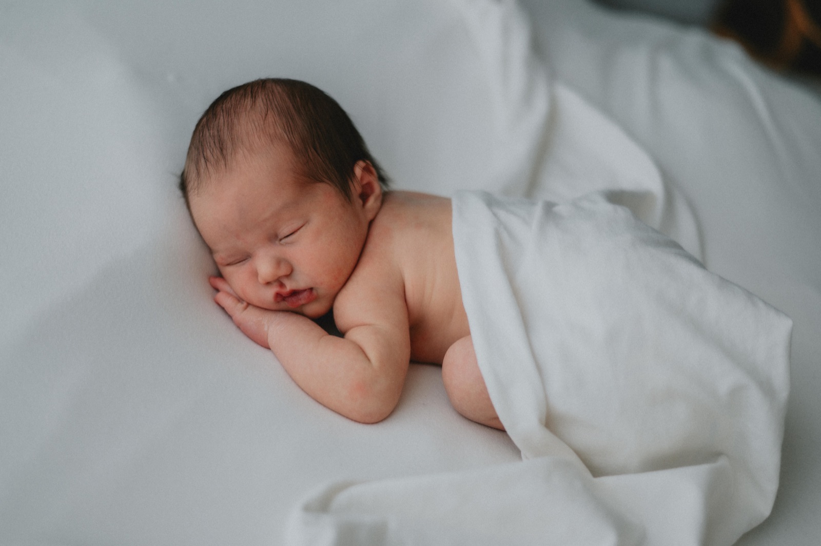 Neonato addormentato avvolto in una fascia chiara