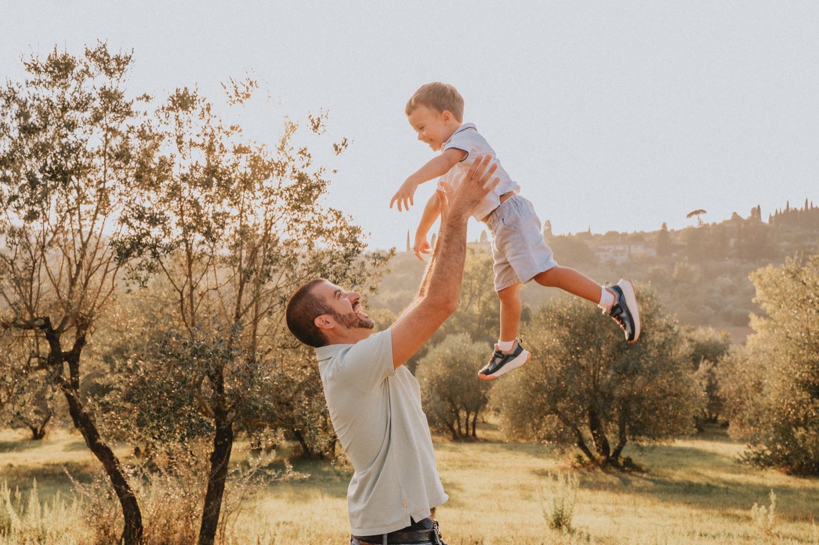 Papà che lancia in aria il bambino in un uliveto