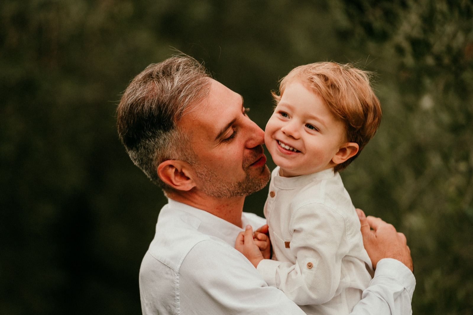 Papà e bambino che si guardano ridendo fra gli ulivi